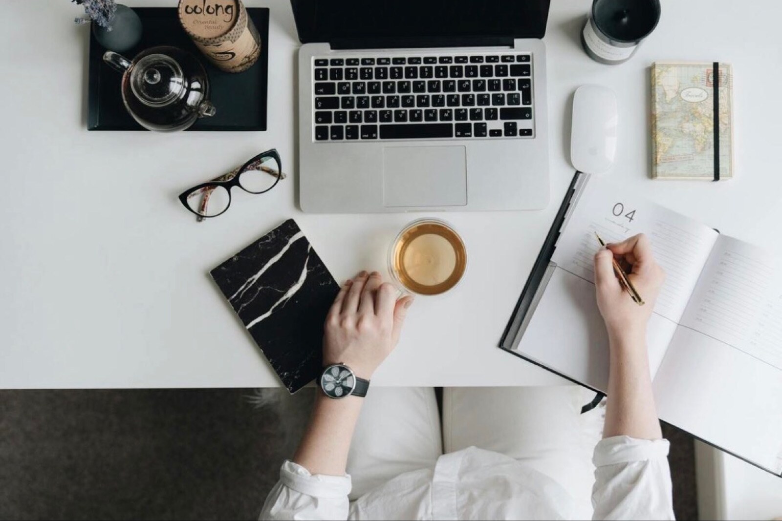 A calm desk flat-lay with a laptop, cup of tea, and a marble notebook.